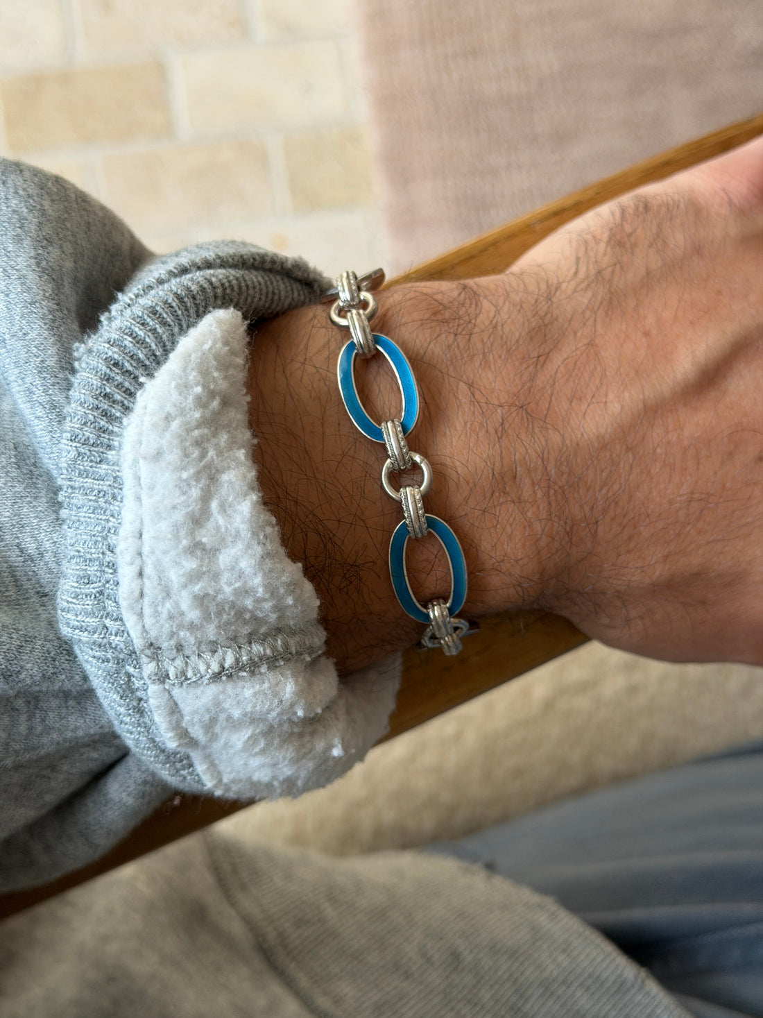 Wrist shot of the blue enamel oval link bracelet against a brick wall background