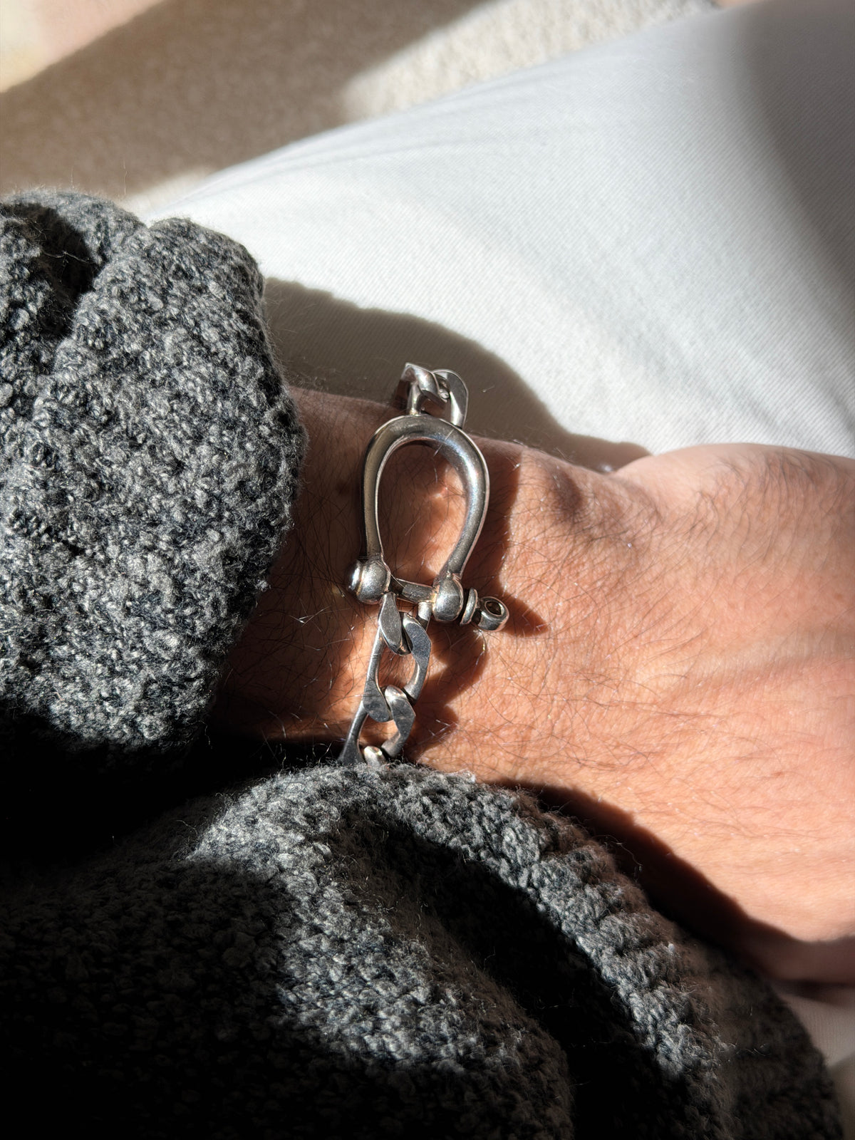 Horseshoe shackle bracelet on the wrist against a gray knit cuff, the domed pin ends and looped screw head catching the light