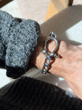 Angled wrist view of the sterling horseshoe bracelet, the polished shackle leading into flat beveled curb links