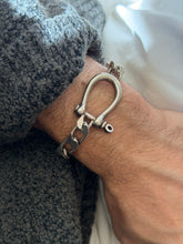 Close view of the silver horseshoe shackle on the wrist, its smooth curved bow, ball shoulders, and threaded crossbar pin