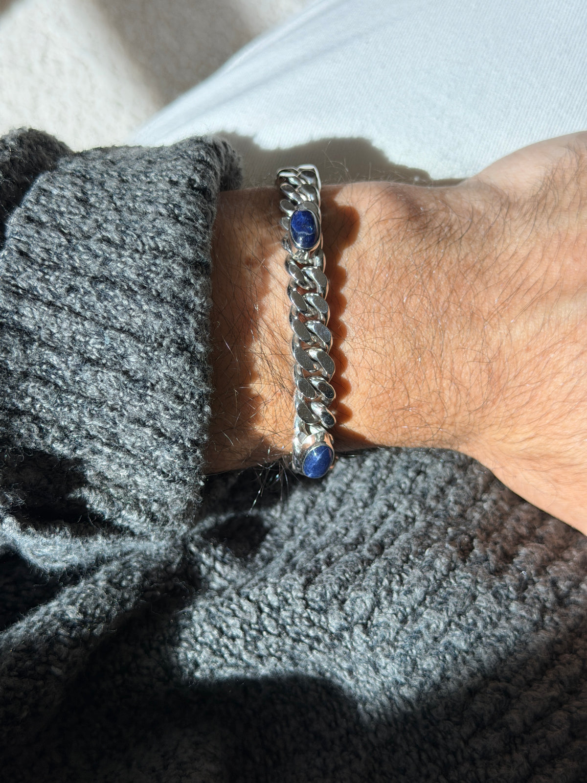 Vintage sterling silver curb chain bracelet set with oval lapis lazuli cabochons in polished bezels, worn on the wrist in sunlight