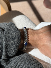 Sterling curb chain bracelet with lapis cabochons on the wrist near a bentwood chair, the stones glowing in raking light