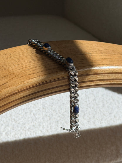 Lapis lazuli and sterling curb bracelet draped over a bentwood oak chair arm, showing three cabochons and the box clasp