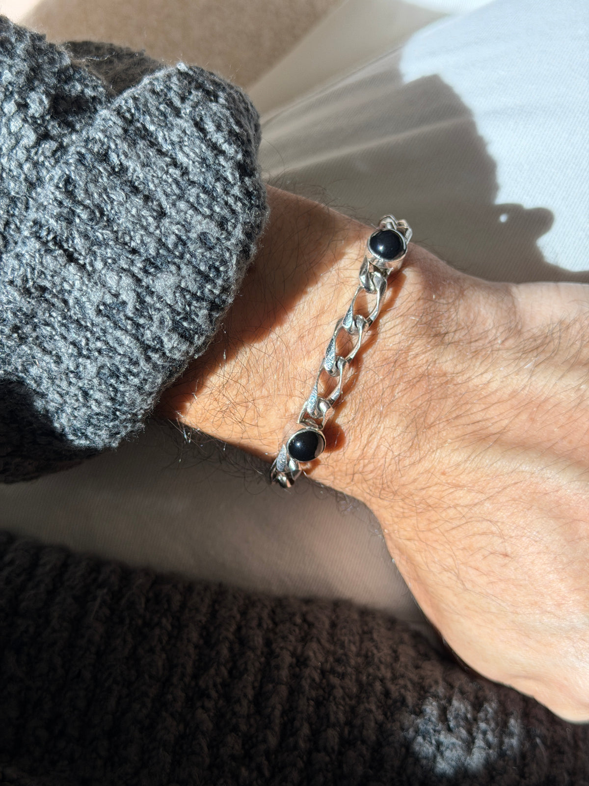 Vintage sterling silver curb chain bracelet with round black onyx cabochons in raised bezels, worn on the wrist in sunlight