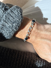 Vintage sterling silver curb chain bracelet with round black onyx cabochons in raised bezels, worn on the wrist in sunlight