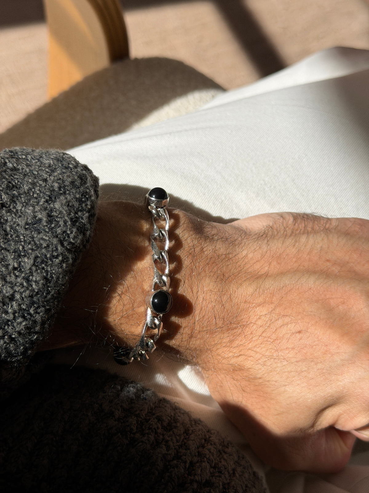 Onyx and silver bracelet on the wrist against cream trousers, the polished black domes set between textured and polished curb links
