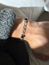 Close wrist view of the onyx cabochon bracelet, showing the open elongated curb links with satin textured faces