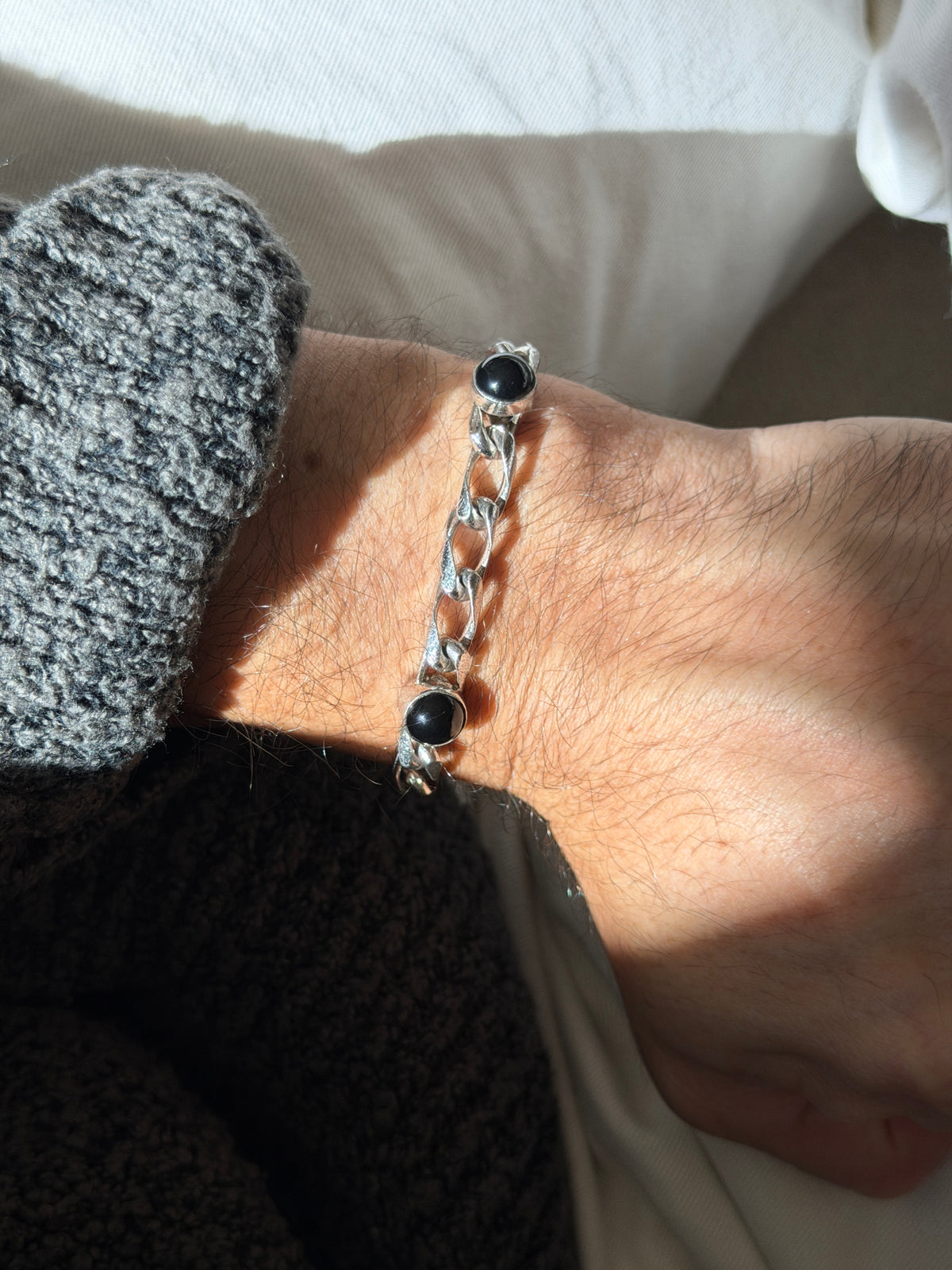 Close wrist view of the onyx cabochon bracelet, showing the open elongated curb links with satin textured faces