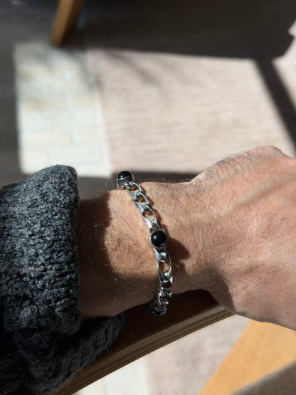 Sterling and onyx curb bracelet on a wrist resting on a wooden chair arm, the black stones reflecting the window light