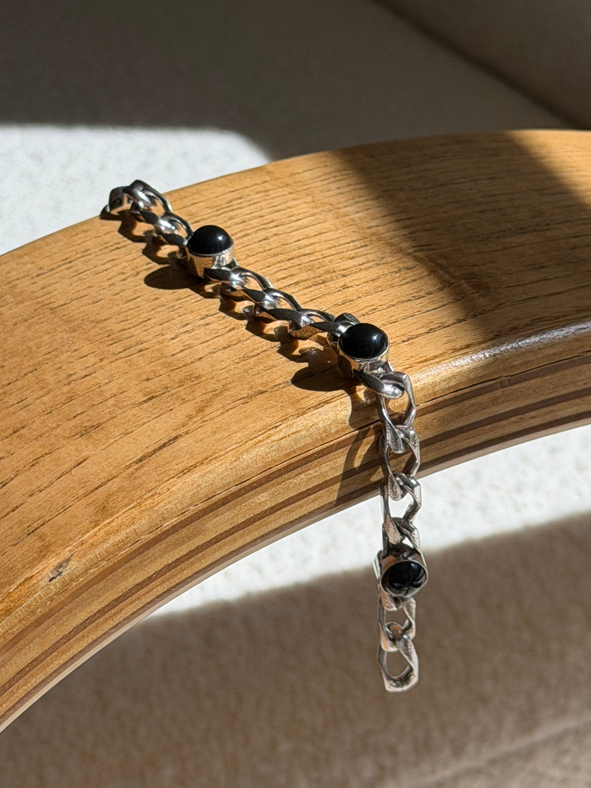 Black onyx cabochon bracelet draped over a bentwood oak chair arm, three domed stones spaced along the textured silver chain