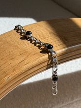 Black onyx cabochon bracelet draped over a bentwood oak chair arm, three domed stones spaced along the textured silver chain