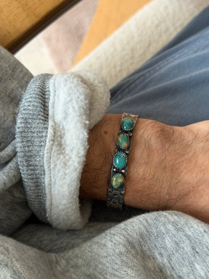 Cuff worn on the wrist over a grey sweatshirt cuff, showing the four turquoise stones and stamped silver design