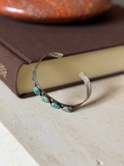 Cuff leaning against the book from the opposite angle, showing its open ends and turquoise stones from the front