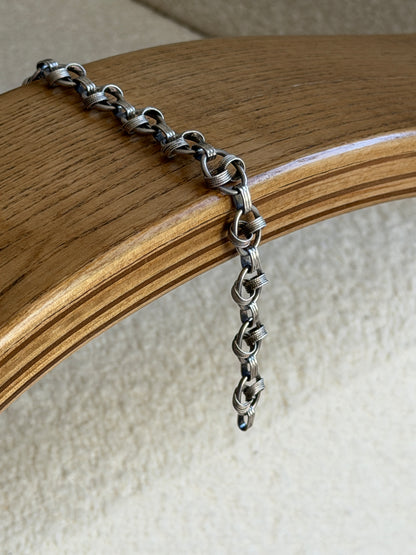 Bracelet draped over the curved edge of a wooden chair arm, showing its fluid articulation