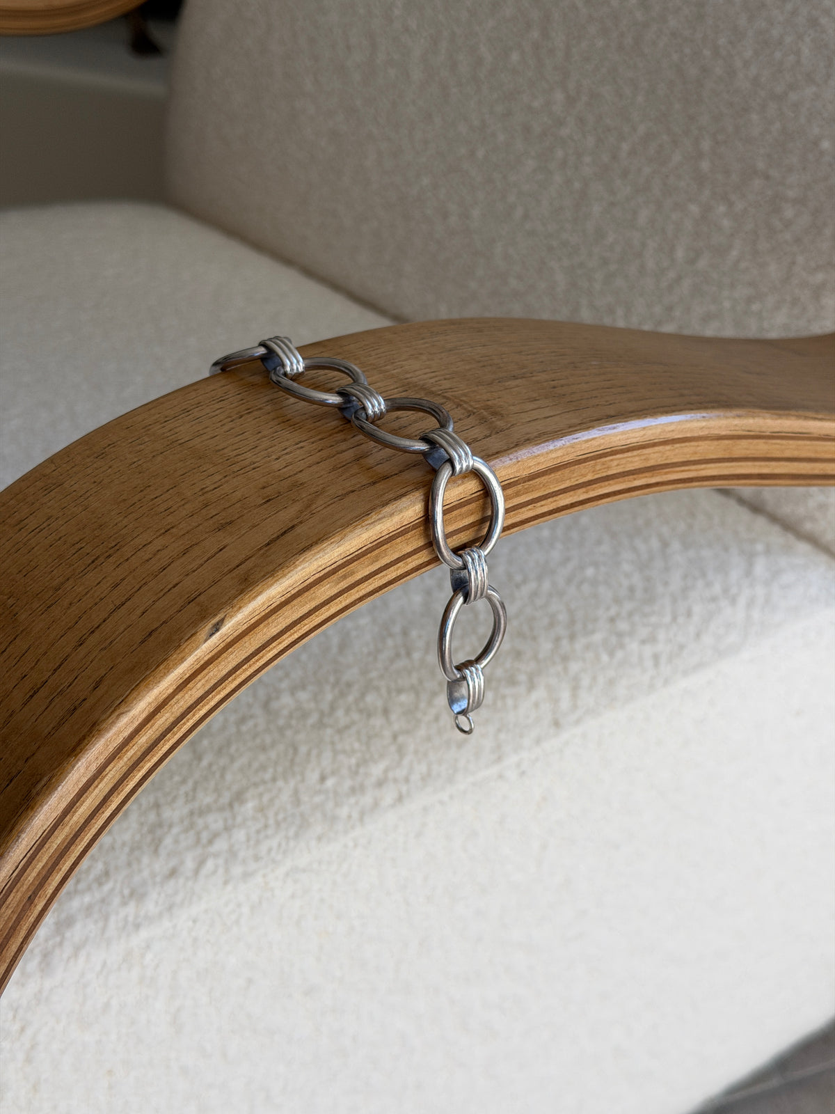 Bracelet draped over the curved edge of a wooden chair arm, showing its sculptural form and clasp