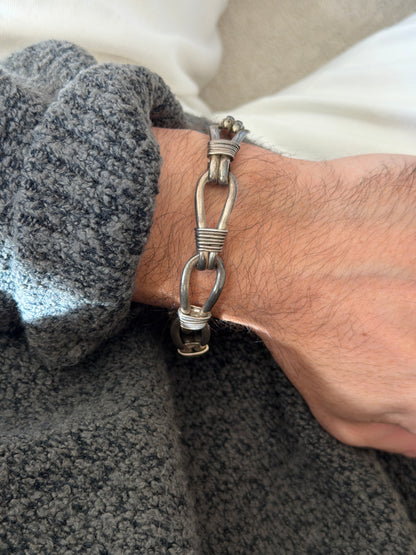 Vintage sterling silver nautical rope link bracelet of elongated teardrop loops bound with coiled wire wraps, worn on the wrist against a gray knit cuff