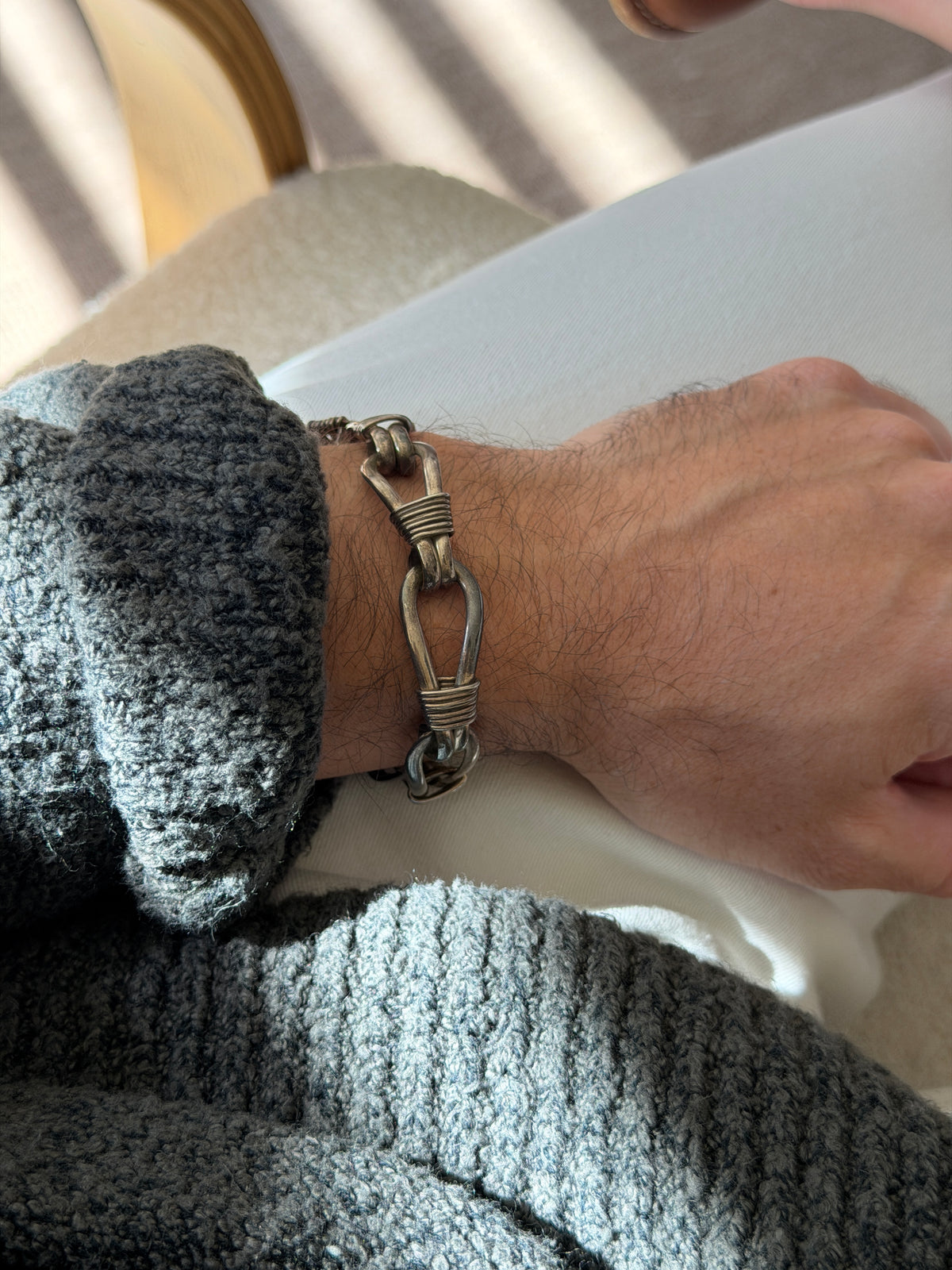 Nautical rope bracelet on the wrist beside a bentwood chair, the wire lashed loops showing a warm oxidized patina