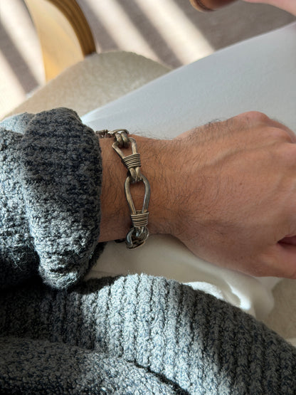 Nautical rope bracelet on the wrist beside a bentwood chair, the wire lashed loops showing a warm oxidized patina