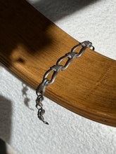 Sterling nautical rope bracelet draped over a bentwood oak chair arm, the lashed loops and hook clasp end hanging free