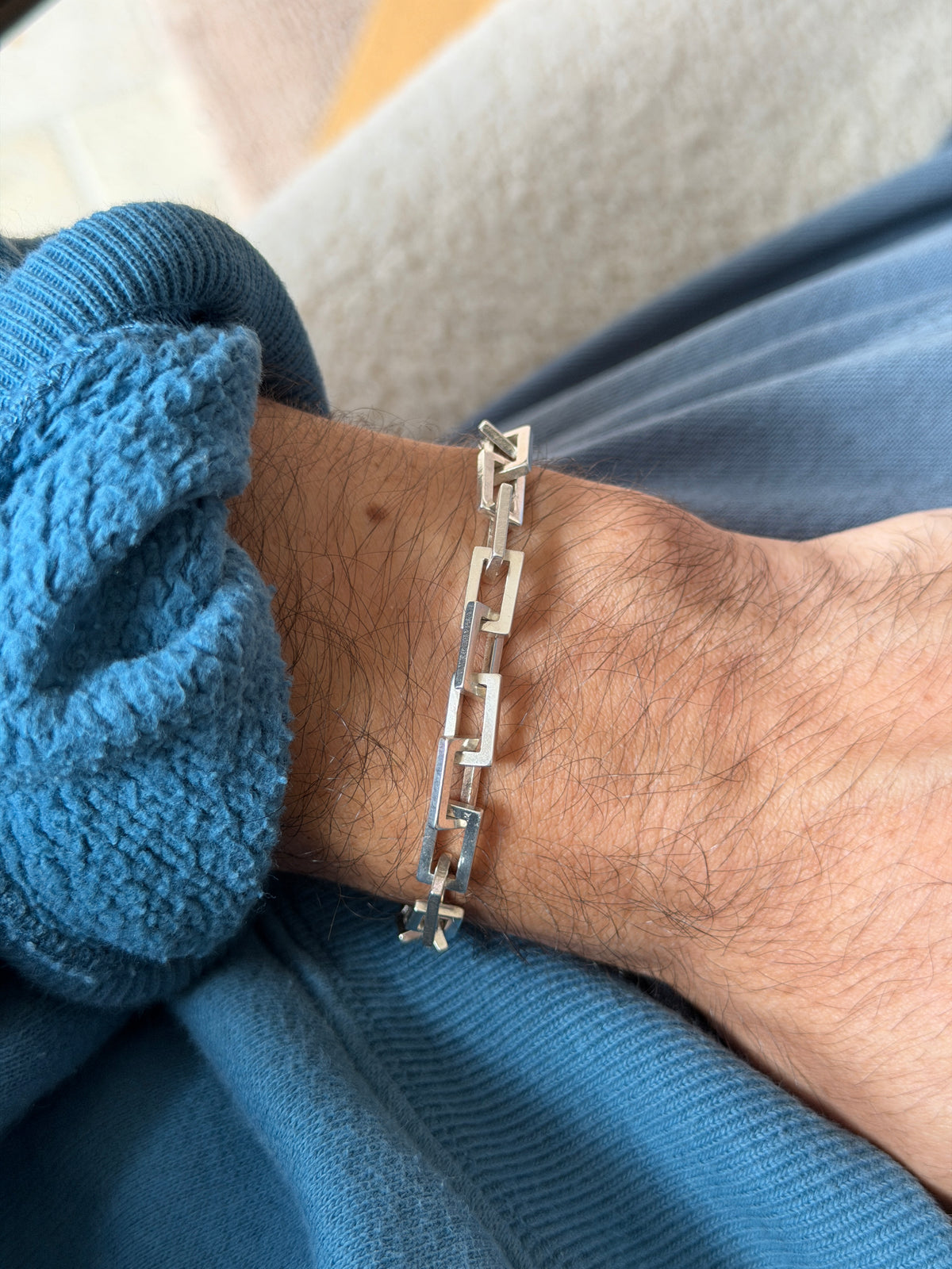 Vintage sterling silver bracelet of open rectangular links with squared edges, worn on the wrist against a blue fleece cuff