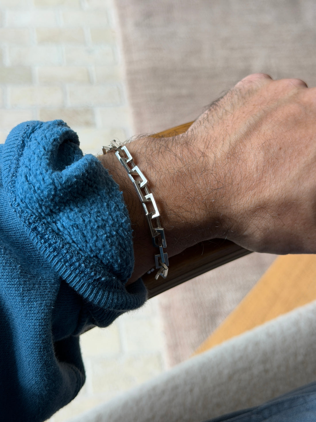 Sterling rectangle link bracelet on a wrist resting on a wooden chair arm, a pale brick wall behind