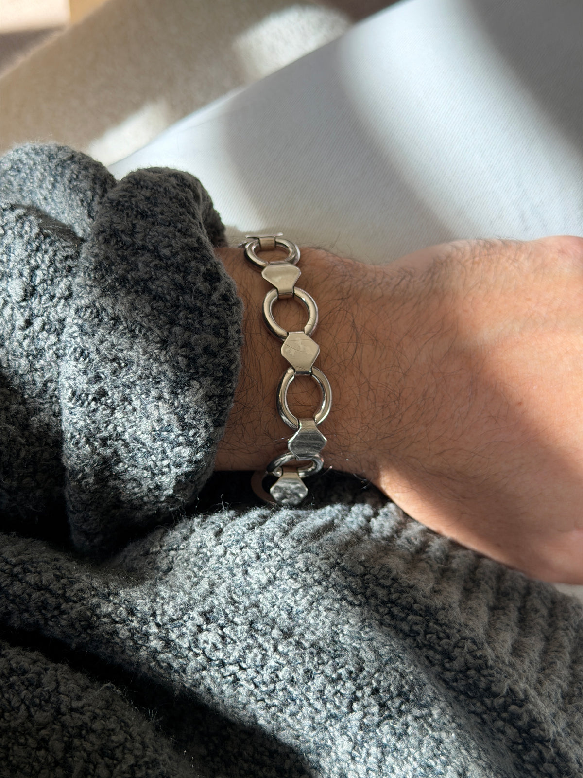 Round and band link bracelet on the wrist in sunlight, the polished rings alternating with angular hexagon connectors