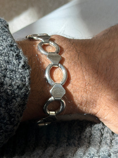 Close wrist view of the sterling round link bracelet, light surface wear visible on the flat hexagonal plates and hinged joints