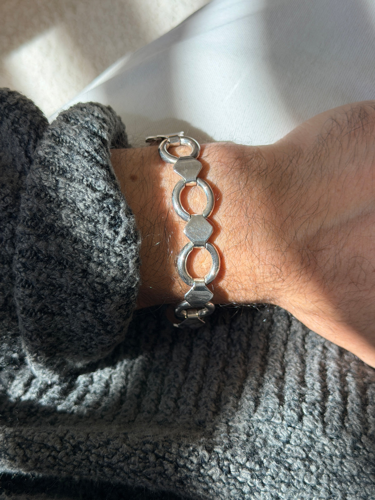Straight on wrist view of the round and band bracelet, the bright silver rings and hexagon bands in raking light