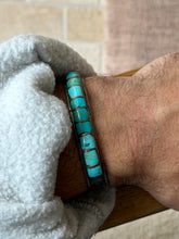 Cuff worn on the wrist against a tiled brick wall background, closer view of the turquoise inlay segments