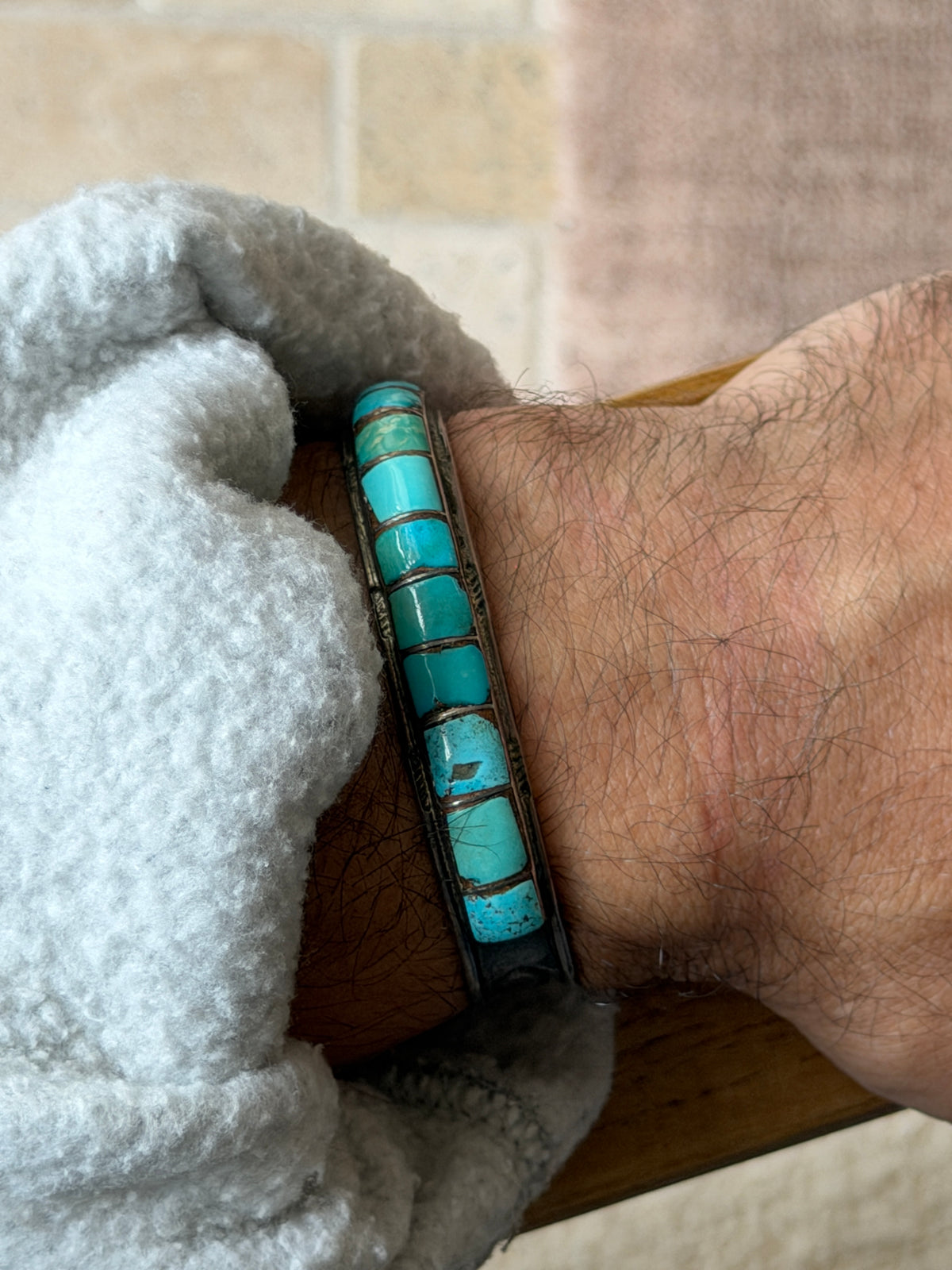 Cuff worn on the wrist against a tiled brick wall background, closer view of the turquoise inlay segments