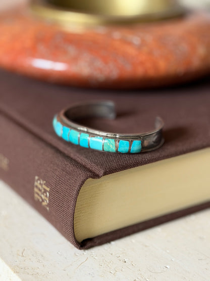 Cuff resting on a dark leather book with a blurred brass object behind it