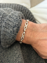 Two tone infinity link bracelet in polished sterling silver with small rose toned gold barrel accents, worn on the wrist against a gray sweater