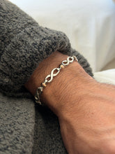 Infinity link bracelet on the wrist, each figure eight silver link joined by short bars and a warm gold bead
