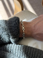Two tone silver and gold bracelet on the wrist beside a bentwood chair, the infinity links reflecting the window light