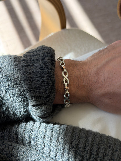 Two tone silver and gold bracelet on the wrist beside a bentwood chair, the infinity links reflecting the window light