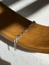 Sterling and gold infinity link bracelet draped over a bentwood oak chair arm, the clasp end hanging below