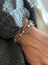 Twisted rope link bracelet on the wrist against a gray knit cuff, the smooth bone shaped bars contrasting with the ribbed ovals