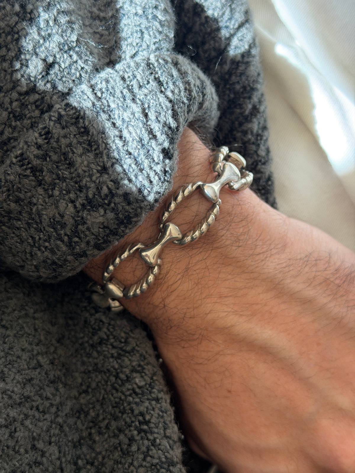 Twisted rope link bracelet on the wrist against a gray knit cuff, the smooth bone shaped bars contrasting with the ribbed ovals