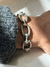 Close view of the twisted rope bracelet on the wrist, the deeply ribbed ovals and polished bone connectors in raking light