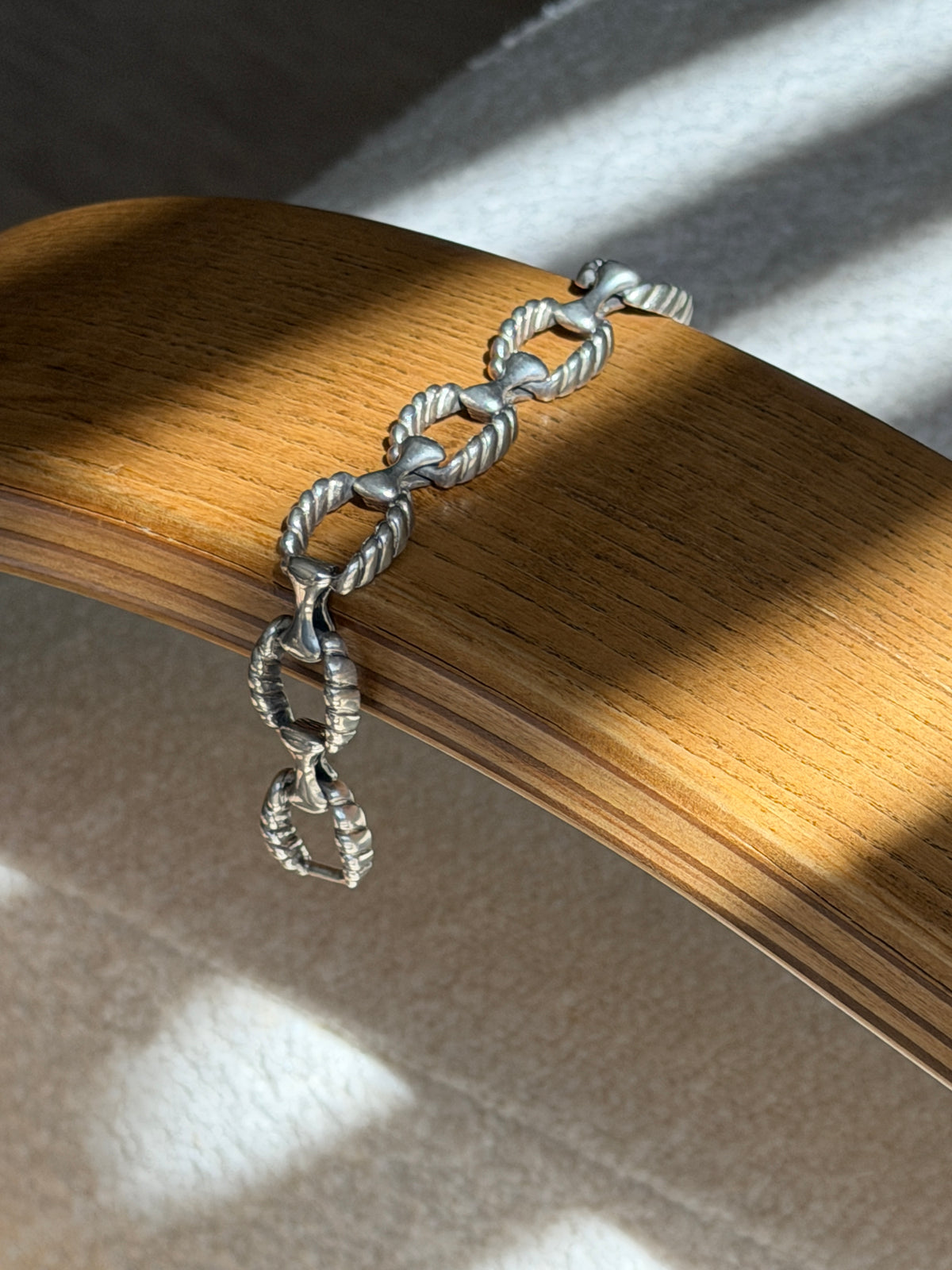Twisted rope and bone connector bracelet draped over a bentwood oak chair arm, the oxidized grooves defining each rope link